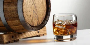 A glass of cask strength whiskey on ice next to a wooden cask.